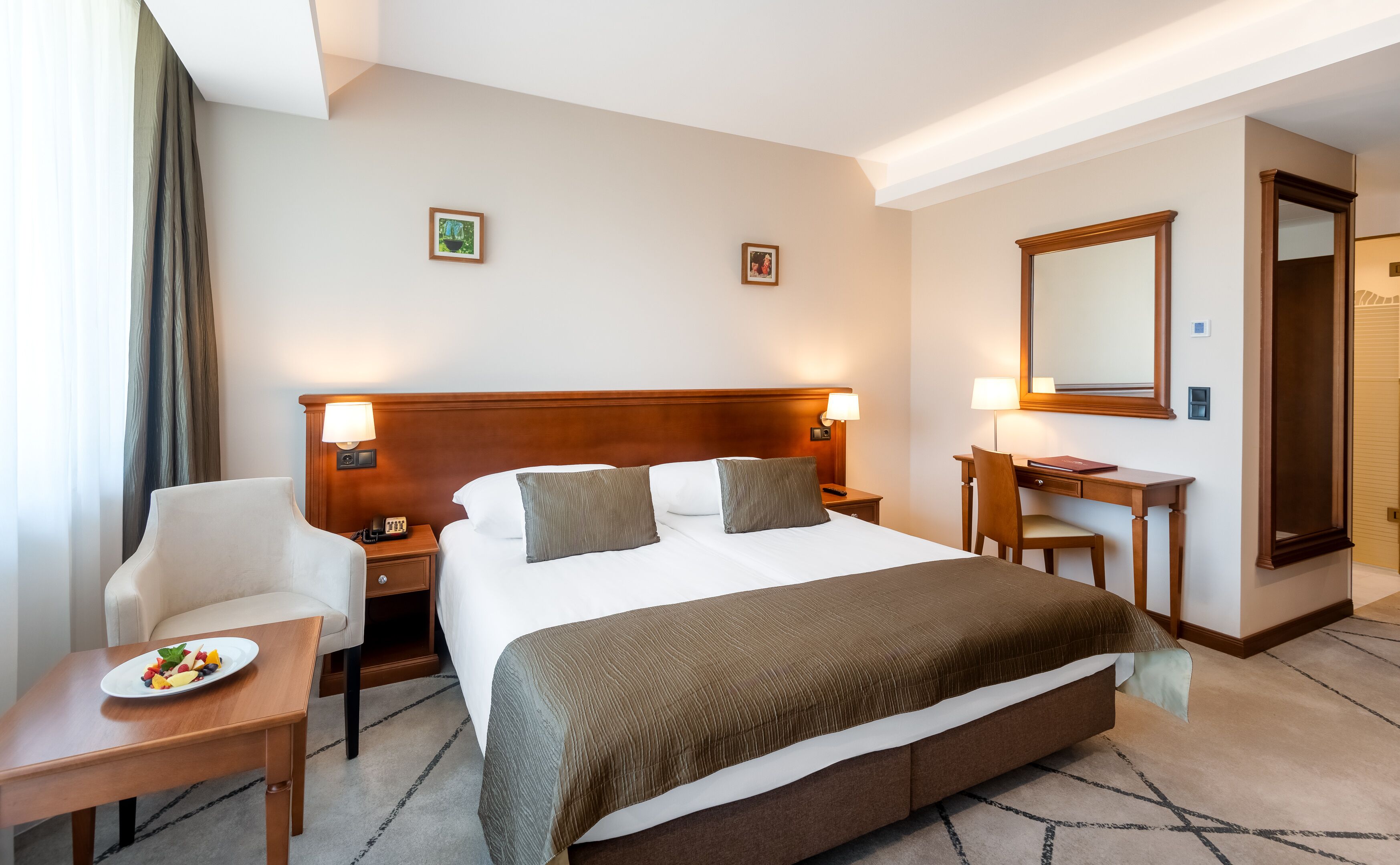 Habitación de hotel con una cama grande, mesitas de noche, un escritorio, una silla y una pequeña mesa con fruta.