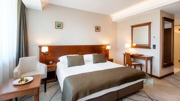 Habitación de hotel con una cama grande, mesitas de noche, un escritorio, una silla y una pequeña mesa con fruta.