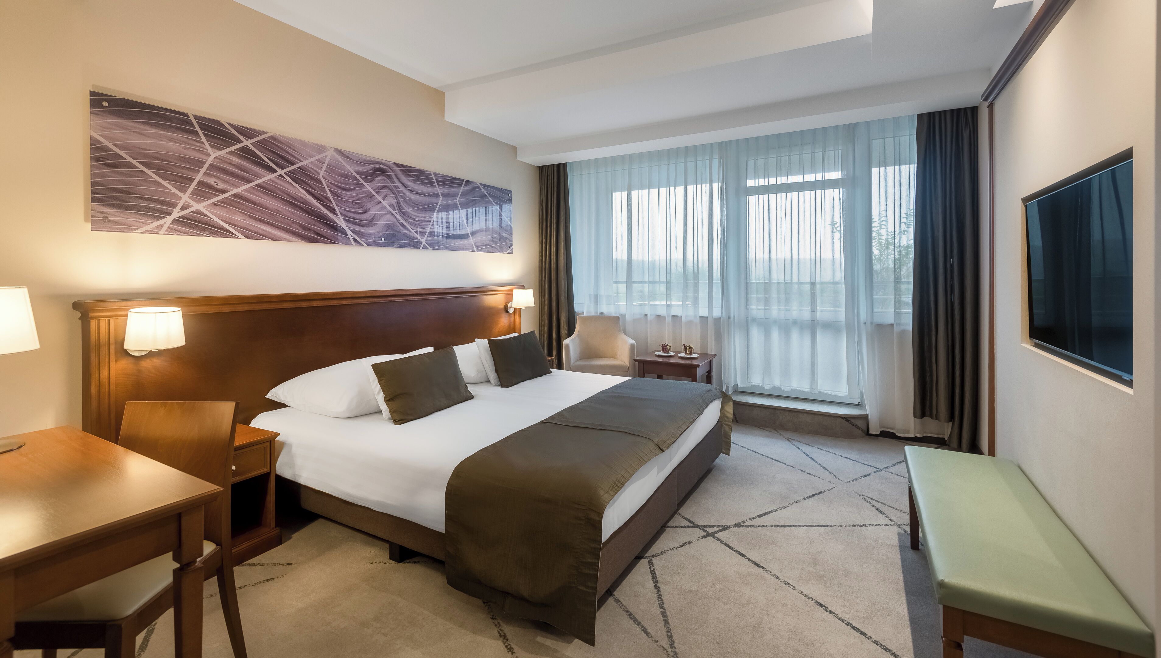 Habitació d'hotel amb un llit gran, escriptori, cadira, televisió i finestra amb cortines.