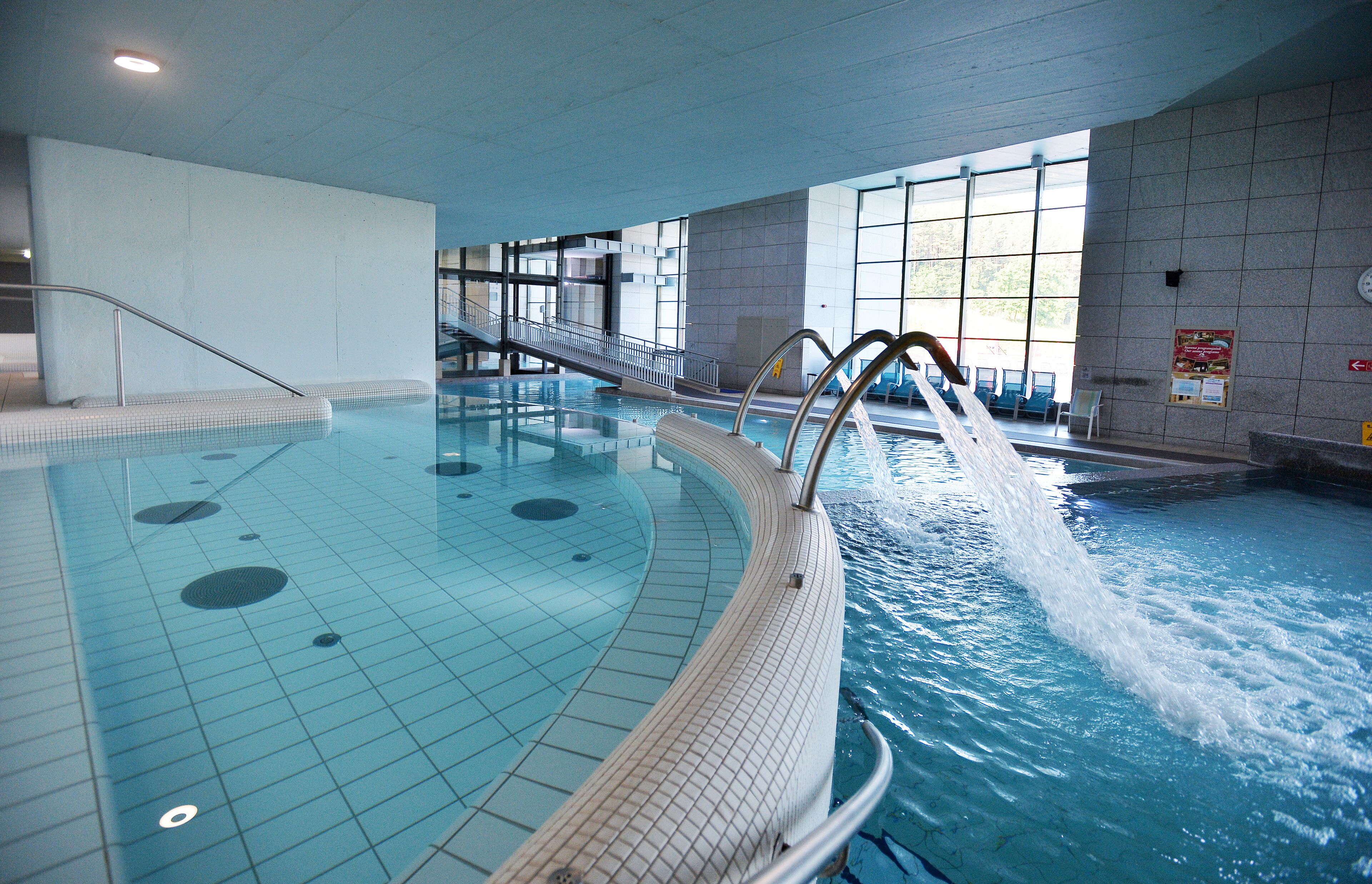 An indoor swimming pool with clear water, a diving board, and a staircase leading to a viewing area.