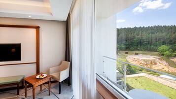 A balcony with a dining area, a TV, and a view of a forested area.