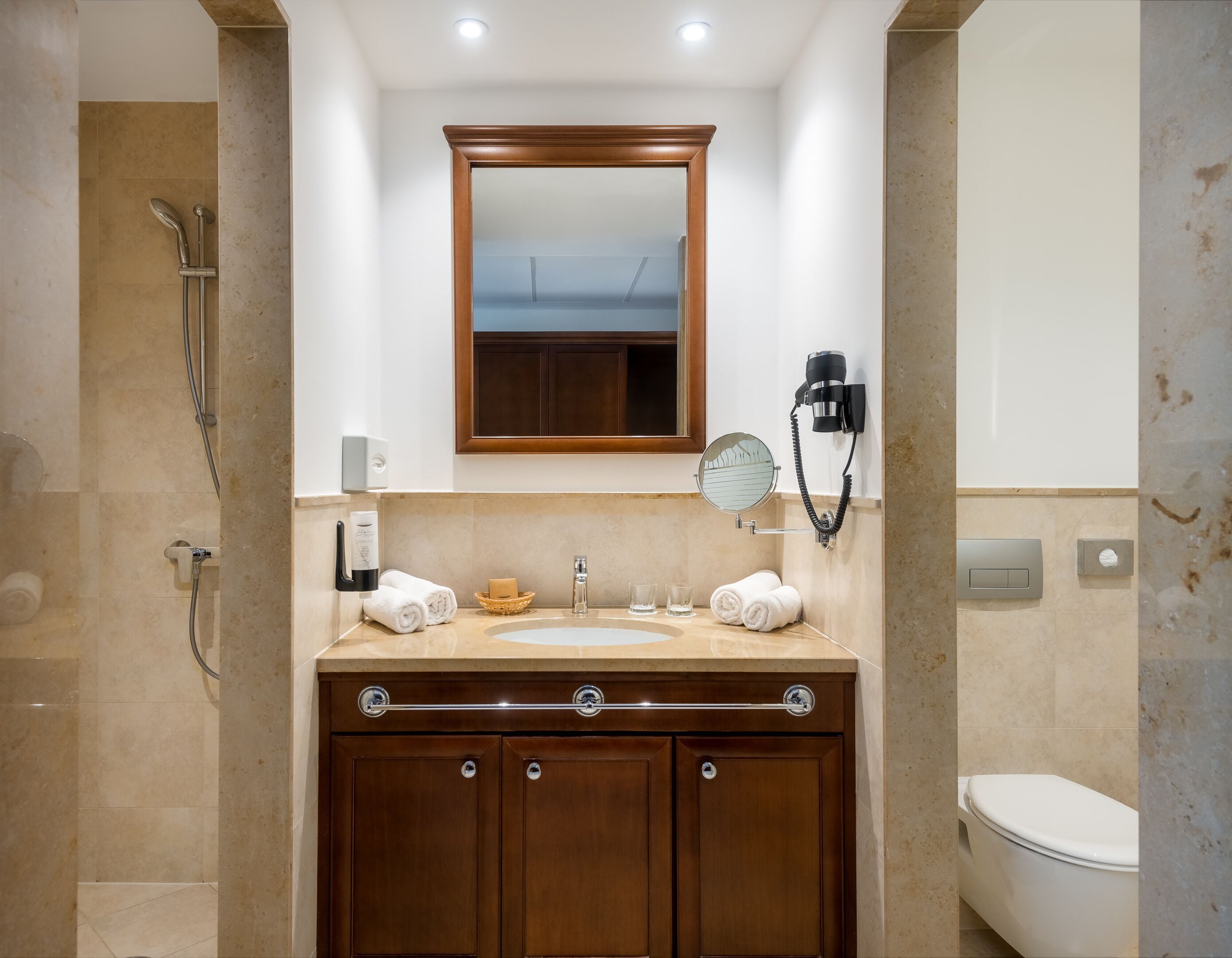 Un baño con tocador de madera, espejo, toallero, secador de pelo y retrete.