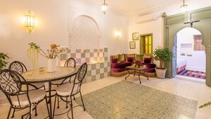 A dining area with a round table and chairs, a sofa, and a coffee table. There are decorative wall tiles and a potted plant. - Private Riad for 4 people In Historic Neighborhood/ 5 minutes to Jemaa El-Fna 

 (Marrakesh)