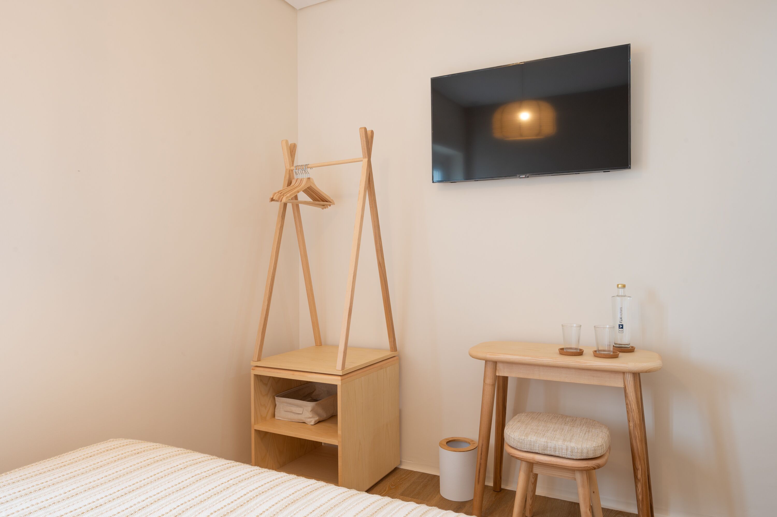 A bedroom with a bed, a wooden bedside table with a lamp, a TV, and a wooden chair.