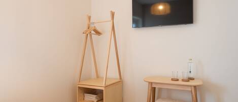 A bedroom with a bed, a wooden bedside table with a lamp, a TV, and a wooden chair.