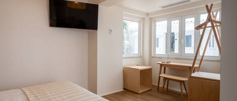 A modern bedroom with a bed, a TV mounted on the wall, a desk with a chair, and large windows.