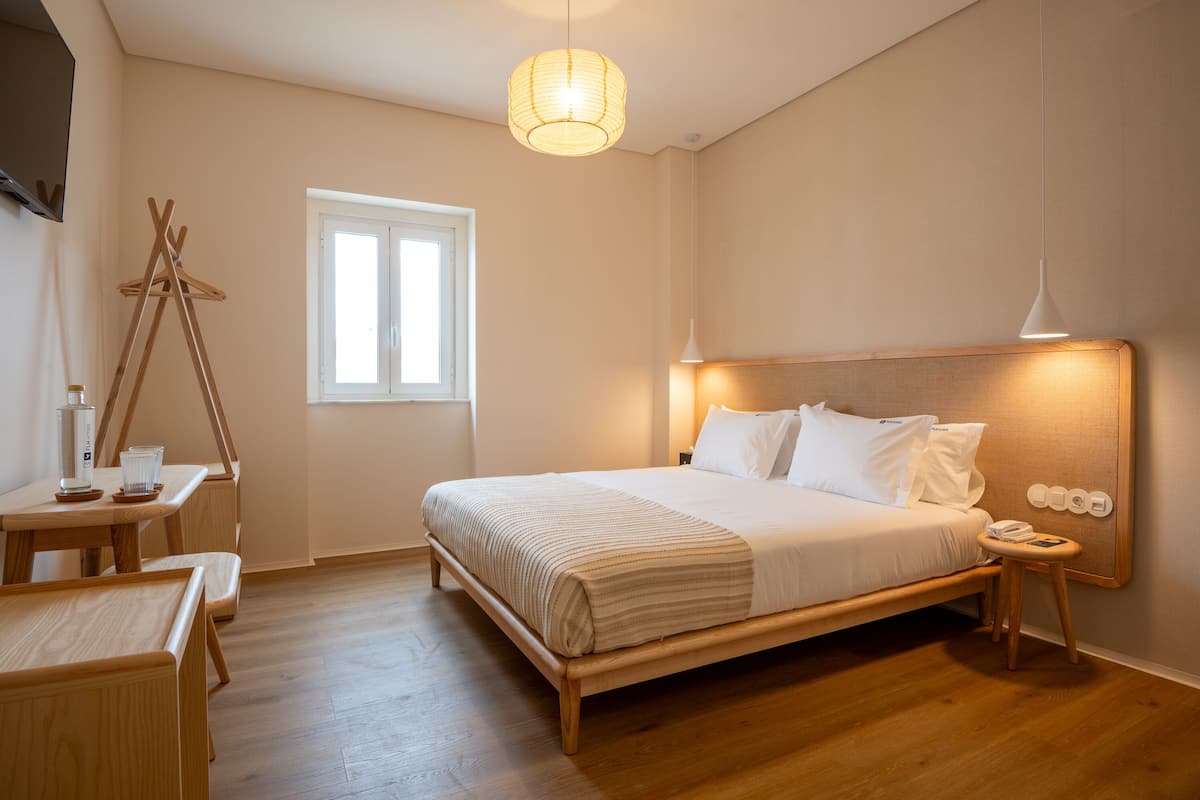 A bedroom with a wooden bed, bedside tables, a hanging lamp, and a window.