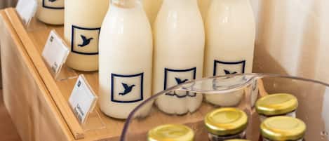 A display of milk bottles with gold caps and labels, arranged on wooden shelves and a glass table.