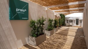 Un área de recepción con un letrero que dice 'praia FLH Hotels' y plantas en macetas a lo largo de un camino empedrado.