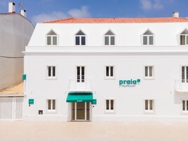 Un edificio blanco con techo de tejas rojas, varias ventanas y un toldo verde con el letrero 'praia FLH Hotels'.