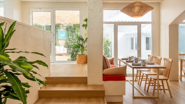 Un comedor amplio con una larga mesa de madera y sillas, un lámpara colgante y vistas a través de grandes ventanales.