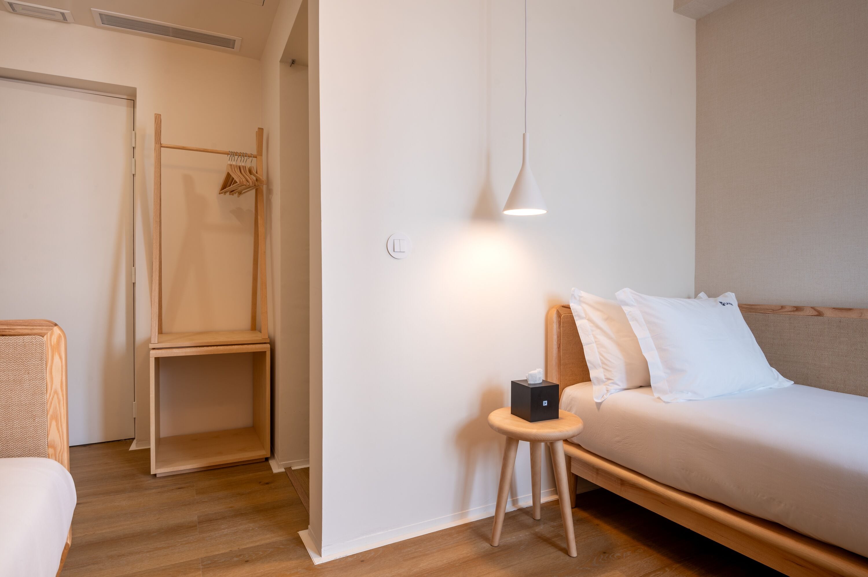 Un dormitorio minimalista con cama de madera, una mesita de noche pequeña, una lámpara colgante y un armario de madera.