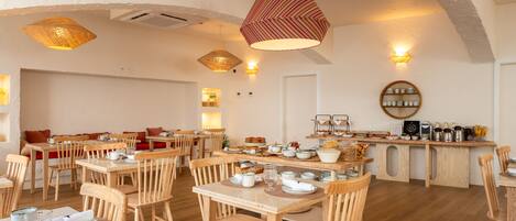 A spacious dining area with wooden tables and chairs, a central bar with various food and drink items, and a cozy seating area with cushions.