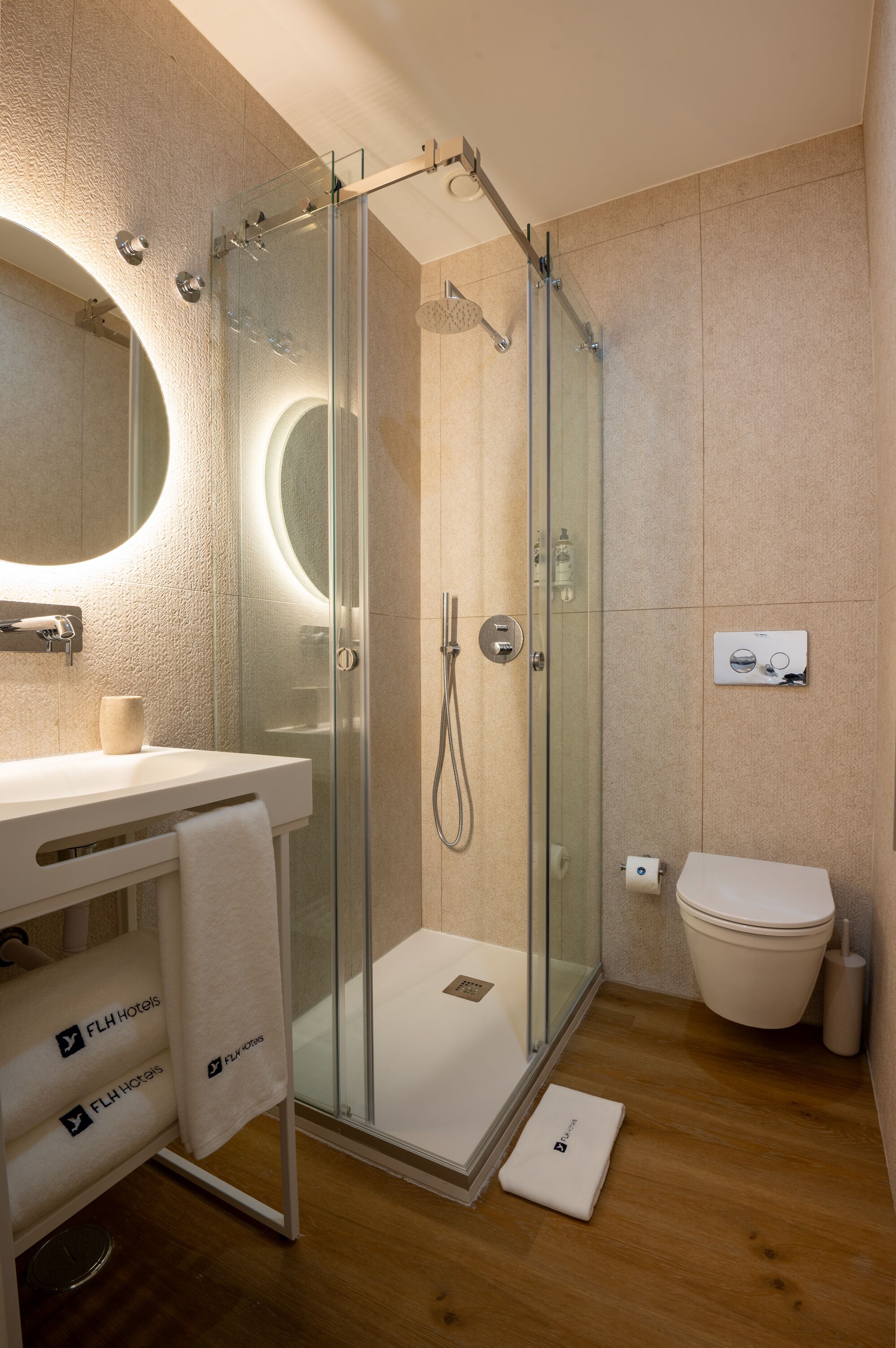 Un baño moderno con cabina de ducha de vidrio, un espejo redondo y un inodoro.