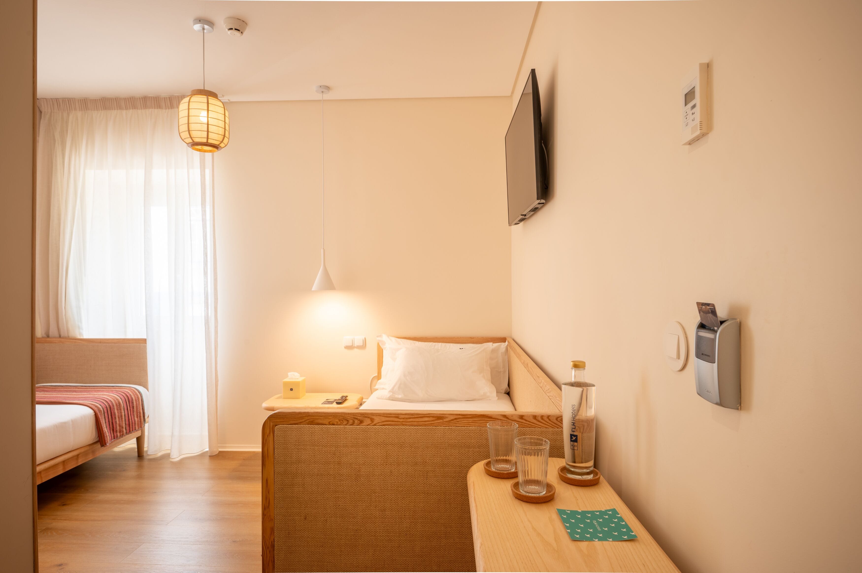 Una camera d'albergo con un letto, un tavolino con bicchieri, una bottiglia e un televisore a parete.