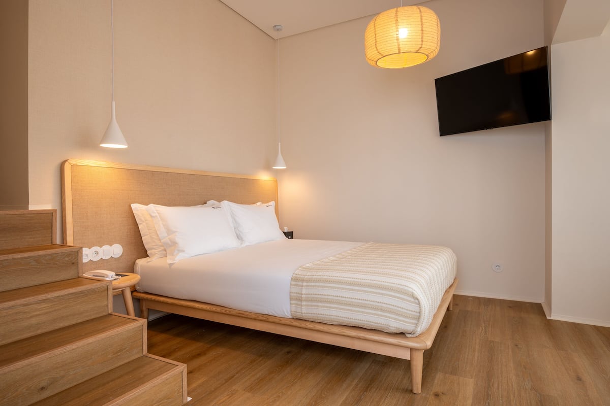 A modern bedroom with a wooden bed, white bedding, a mounted TV, and a wooden staircase.