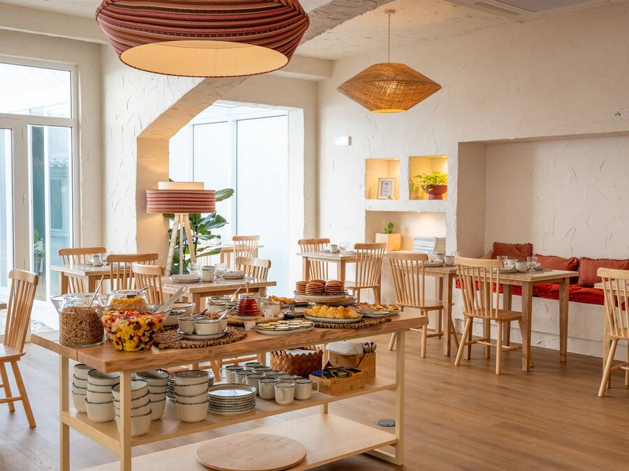 A bright dining area with wooden tables and chairs, a buffet with various dishes, and a large window providing natural light.
