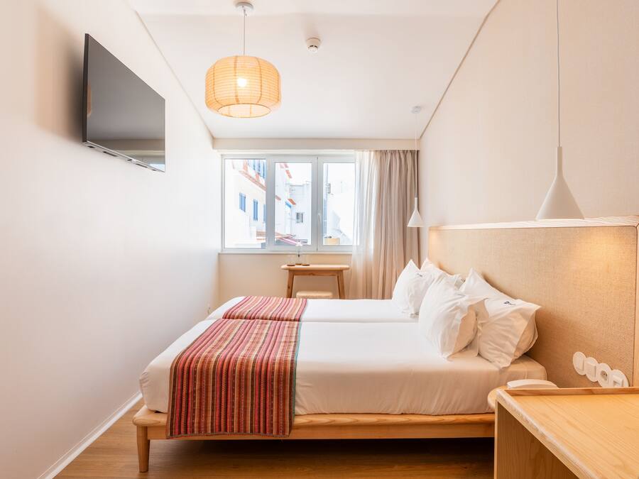 A hotel room with a bed, bedside table, lamp, and a TV mounted on the wall.