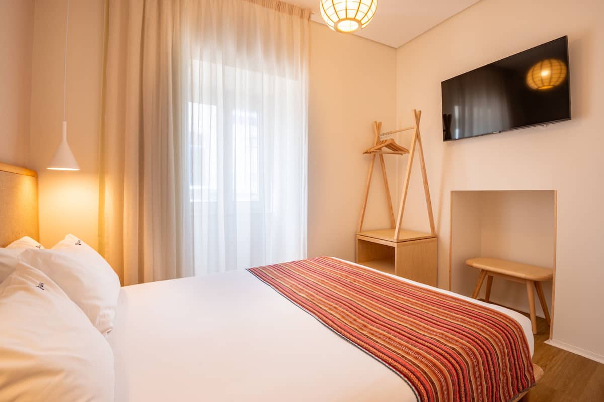 A hotel room with a bed, a TV mounted on the wall, a wooden chair, and a small table.