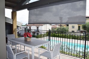 A balcony with a table and chairs, a pool in the background, and a view of neighboring houses. - La Bella Vita, a new three-room apartment with a pool, just a few minutes from Lake Garda. (Boschetti)
