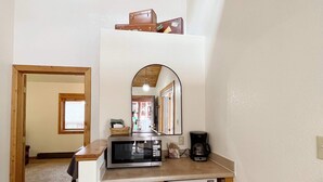Una cucina compatta con forno a microonde, macchina del caffè e piccolo frigorifero. Soffitto in legno e zona soppalco sopra la cucina.