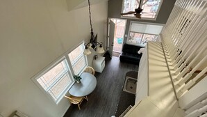 A high-ceilinged room with a dining area, a small kitchen, and a staircase. - Tiny home Within Campground (Woodland Park)