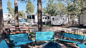 A campground with blue benches, a fire pit, and RVs. - Tiny home Within Campground (Woodland Park)
