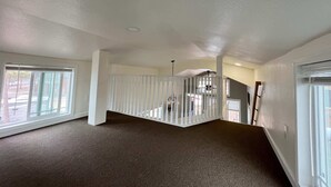 A spacious room with a high ceiling, large windows, and a staircase with a railing. - Tiny home Within Campground (Woodland Park)