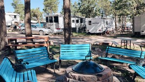 A campground with blue benches, a fire pit, and RVs.
