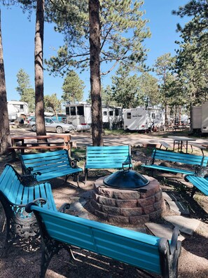 A campground with blue benches, a fire pit, and RVs.