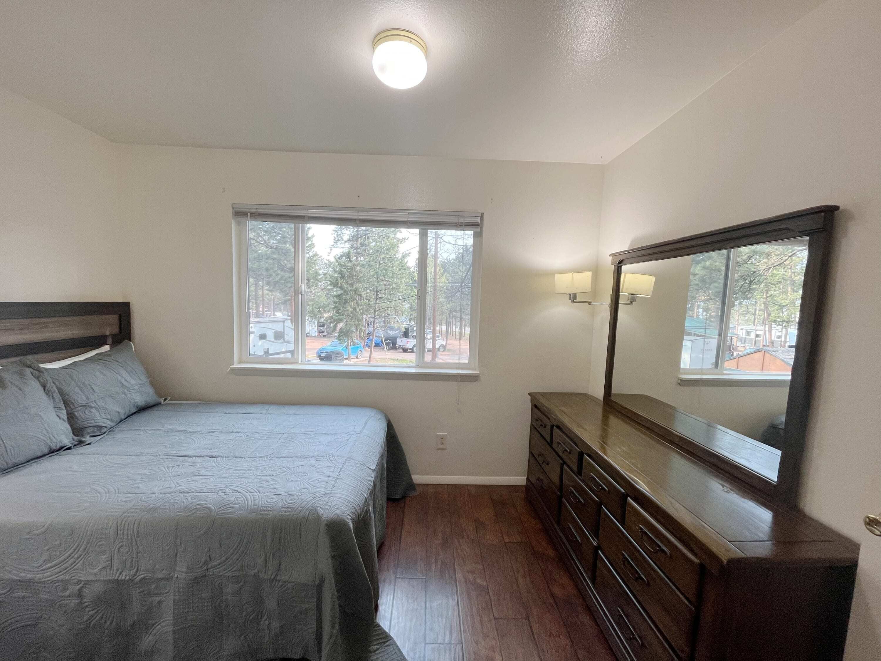 Ein Schlafzimmer mit Bett, Kommode, Fenster und Deckenleuchte.