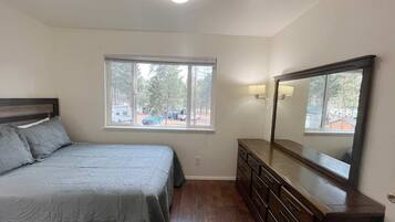 Een slaapkamer met een bed, dressoir, raam en een plafondlamp.