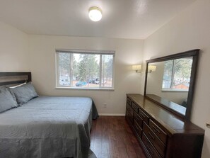 A bedroom with a bed, dresser, window, and a ceiling light. - Two Bedroom Cabin Suite Bed & Breakfast (Woodland Park)