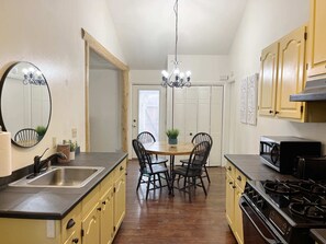 A kitchen with a dining table, chairs, a sink, cabinets, a stove, and a chandelier.