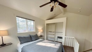 A bedroom with a bed, a window, a ceiling fan, a nightstand, a lamp, a closet, and a radiator.