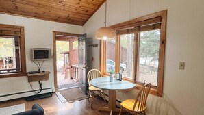 A dining area with a wooden table and chairs, a ceiling fan, and large windows with a view of the outdoors. - Cabin Suite Bed & Breakfast (Woodland Park)