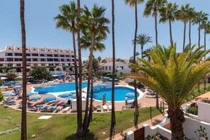 A resort with a central swimming pool, palm trees, and a building with multiple balconies.