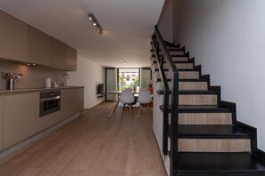 A modern kitchen with wooden flooring, a dining area with two chairs, and a staircase with black railings.