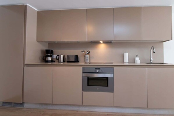 A modern kitchen with a built-in oven, a coffee maker, and a kettle.