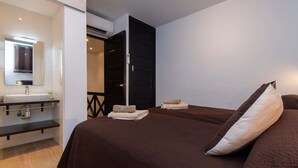 A modern bedroom with a large bed, a bedside table, a mirror, and a bathroom with a sink and towel rack. - Parque Santiago II 87 - Two Bed (Playa de la Américas)
