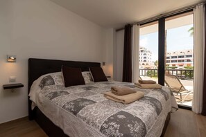 A hotel room with a large bed, a balcony with a chair, and a view of buildings. - Parque Santiago II 87 - Two Bed (Playa de la Américas)