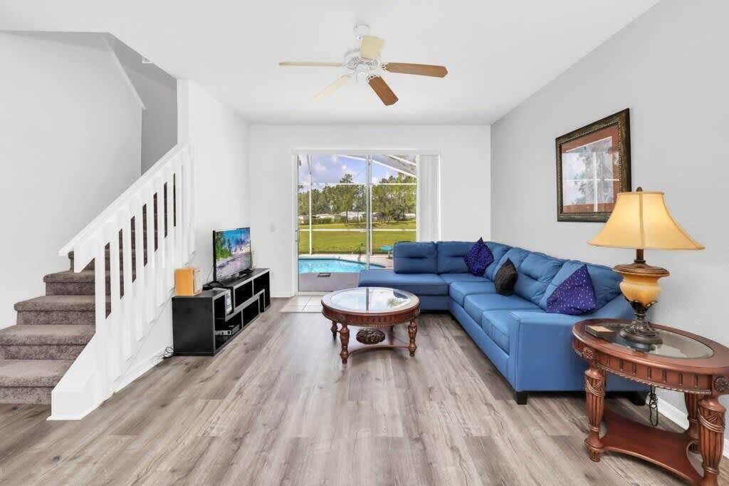 Ein Wohnzimmer mit blauem Sofa, Couchtisch, Fernseher und Deckenventilator.