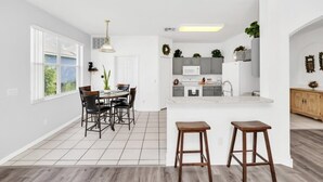 Une cuisine moderne avec des meubles blancs, un îlot central et un coin repas comprenant une table et des chaises.