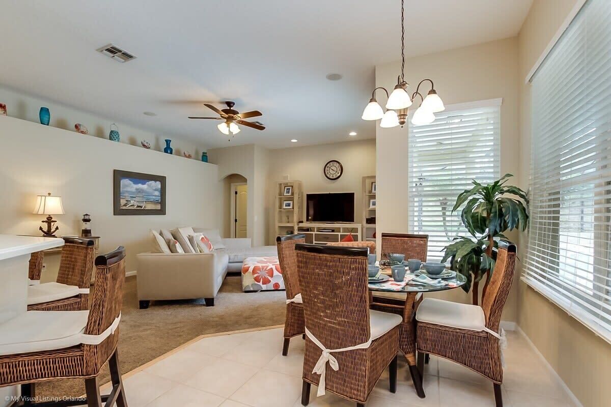 A spacious living room with a dining area, a ceiling fan, and a large window with blinds.