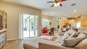 Ein geräumiges Wohnzimmer mit einer großen Couch, einem Couchtisch und einem Deckenventilator. Eine Glastür führt auf einen Balkon.