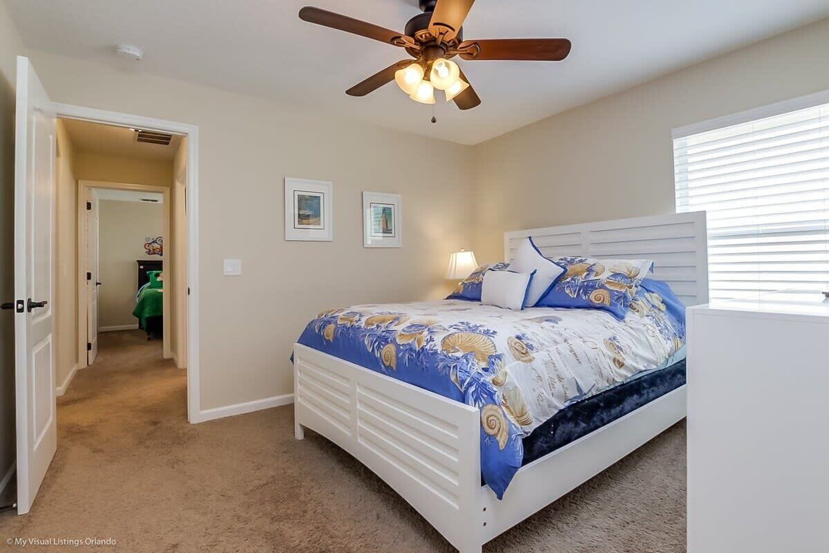 A bedroom with a bed, ceiling fan, and a window with blinds.
