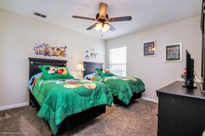 A bedroom with two beds, a ceiling fan, a dresser, and wall decorations.