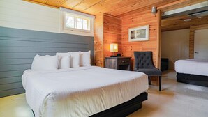 Un dormitorio tipo cabaña de madera con una cama grande, una cama más pequeña, un escritorio con lámpara y una silla.
