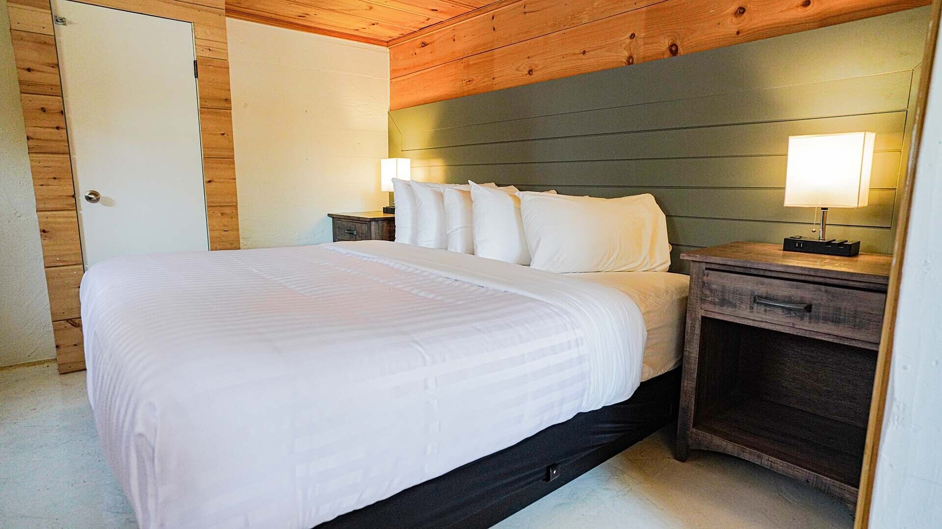 Un dormitorio con una cama, una mesita de noche, una lámpara y un cabecero de madera.