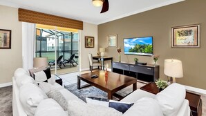 Ein modernes Wohnzimmer mit Sofa, Couchtisch, Fernseher und einem Balkon mit Gartenmöbeln.